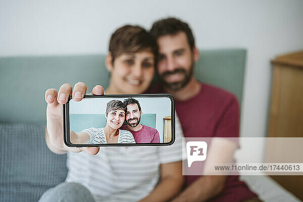 Woman taking selfie with man through smart phone at home