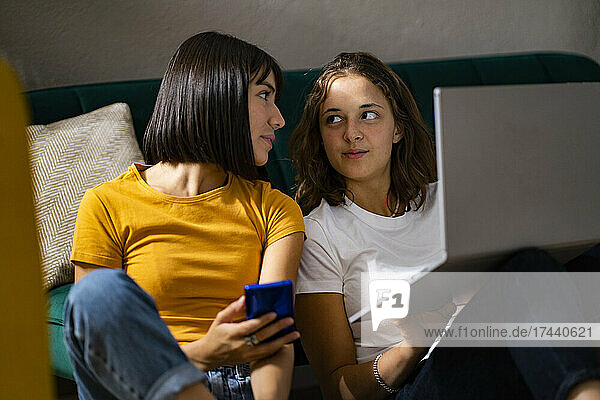 Lesbian couple with mobile phone and laptop looking at each other