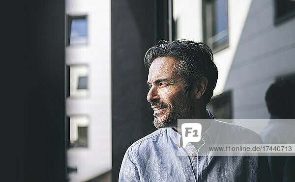 Smiling businessman with hair stubble looking through window