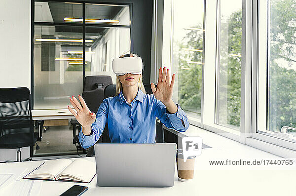 Geschäftsfrau gestikuliert  während sie im Büro ein Virtual-Reality-Headset trägt