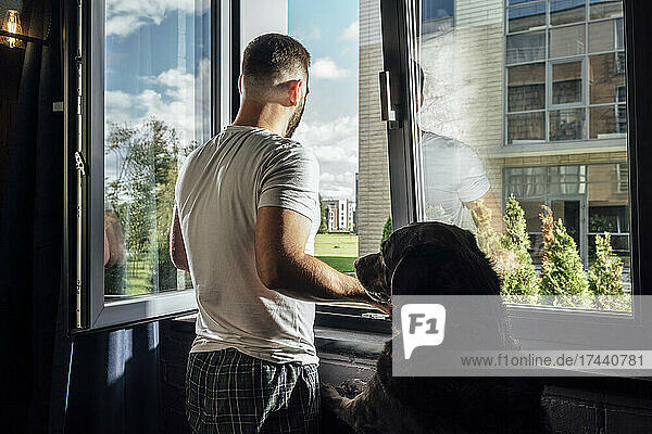 Mid adult man looking through window by dog at home