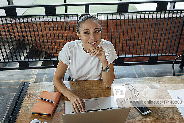 Smiling businesswoman with hand on chin sitting at desk in office