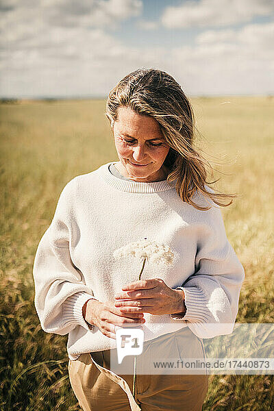 Smiling blond woman looking at flower during sunny day