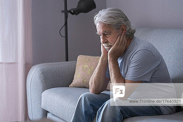 Sad man with hands on chin sitting at home