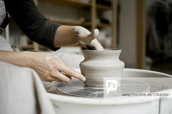 Young craftswoman making flower pot on pottery wheel