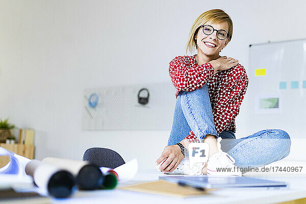 Mid adult businesswoman smiling while sitting on desk