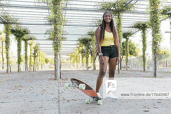 Smiling woman standing with skateboard on footpath