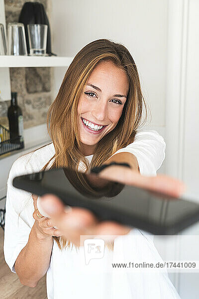 Smiling woman with brown hair giving smart phone at home