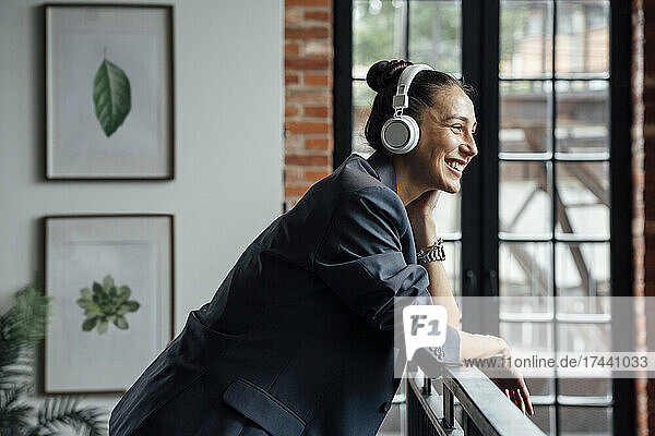 Happy businesswoman listening music through wireless headphones in office