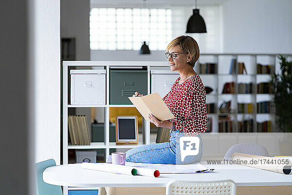 Eine berufstätige Frau mittleren Alters schreibt Tagebuch  während sie am Schreibtisch sitzt