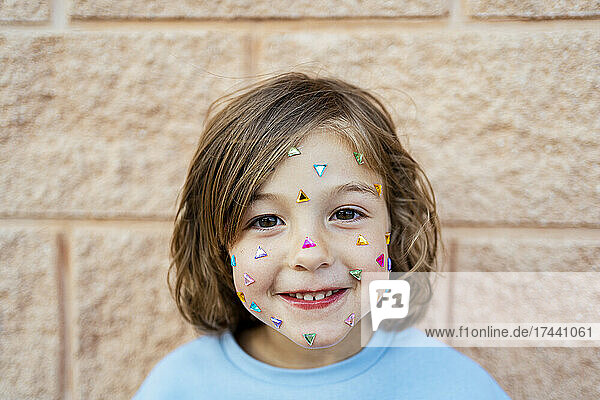 Cute smiling girl with confetti sticking on face in front of wall