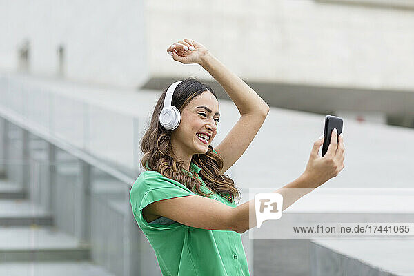 Happy woman with wireless headphones taking selfie through smart phone