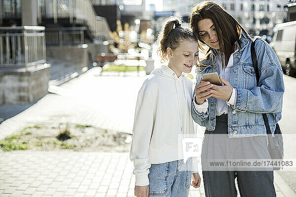 Mother sharing mobile phone with daughter at city street