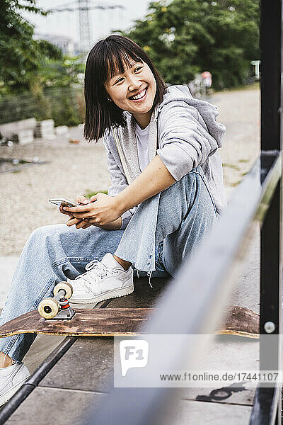Happy female teenager with smart phone sitting on bench