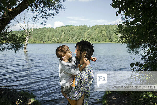 Father looking at son while standing by lake in forest