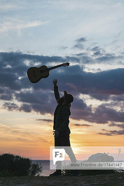 Man throwing guitar while standing on beach during sunset