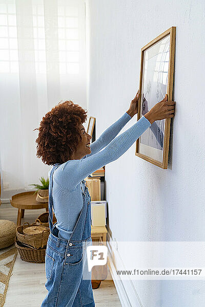 Afro woman hanging picture frame on living room wall