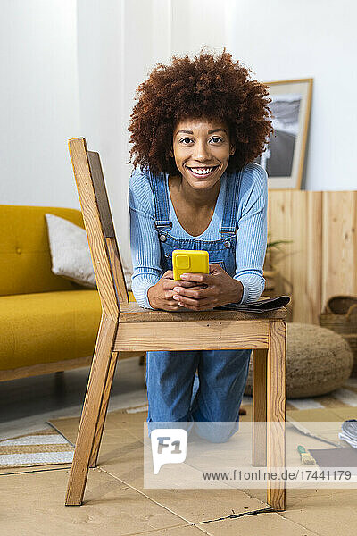 Redhead woman with smart phone leaning on chair at home