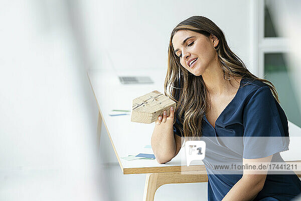 Berufstätige Frau hält Holzhausmodell im Büro