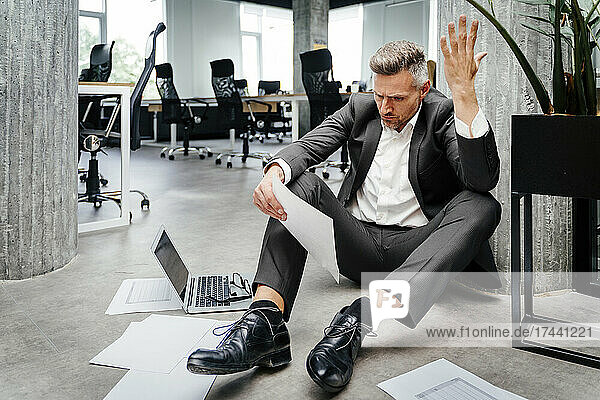 Frustrated businessman gesturing while looking at document in office