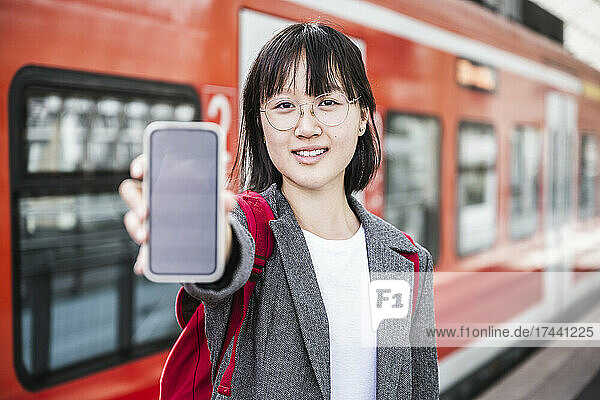 Teenage girl showing smart phone at train station