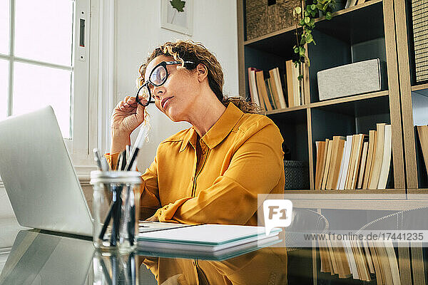 Geschäftsfrau mit geschlossenen Augen  die am Schreibtisch eine Brille abnimmt