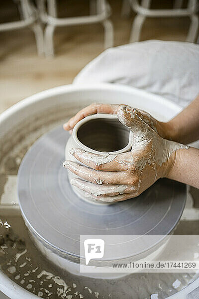Young female potter molding clay on pottery wheel