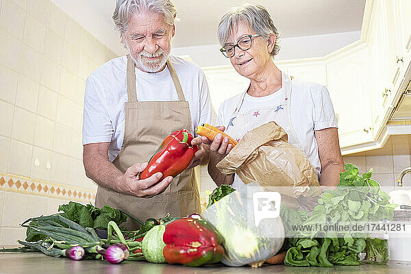 Senior couple removing vegetables from paper bag in kitchen