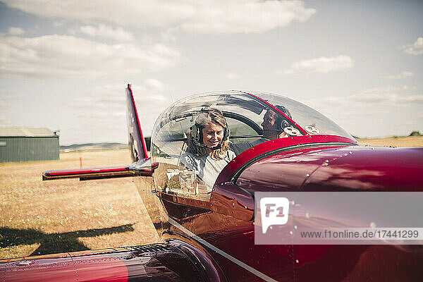 Smiling mature woman piloting airplane during sunny day