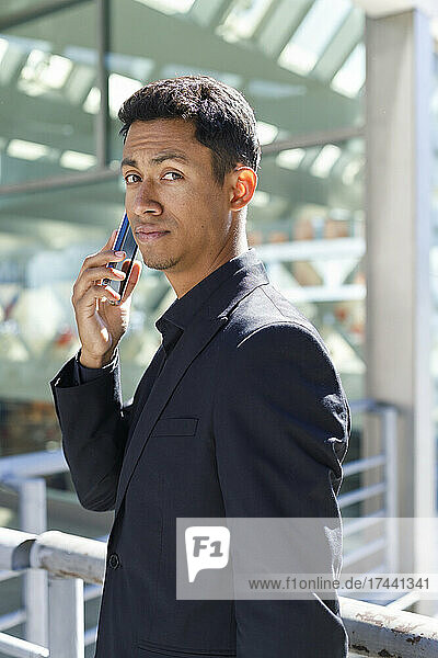 Handsome male professional talking on mobile phone while standing in front of office building