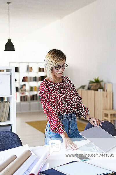 Lächelnde Geschäftsfrau öffnet Laptop am Schreibtisch