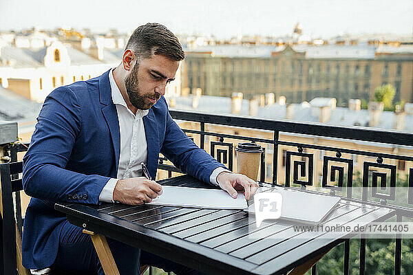 Businessman writing on paper while sitting in balcony