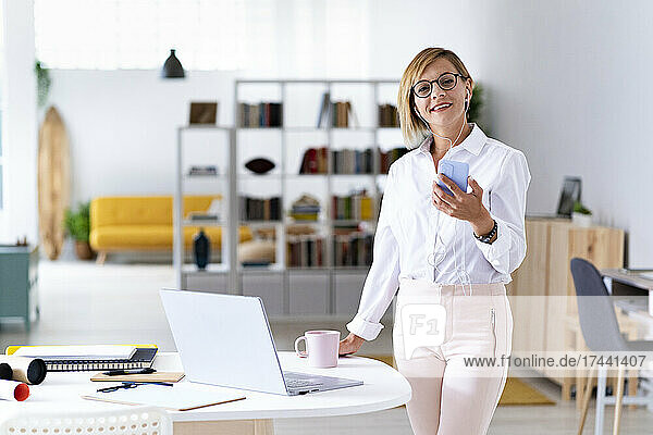 Smiling female professional wearing eyeglasses while holding smart phone at desk