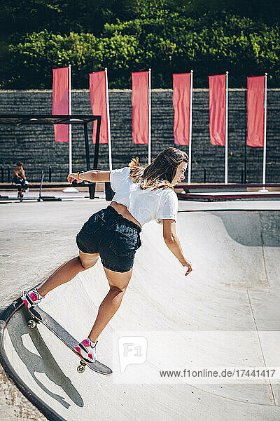 Woman skateboarding at skatepark on sunny day