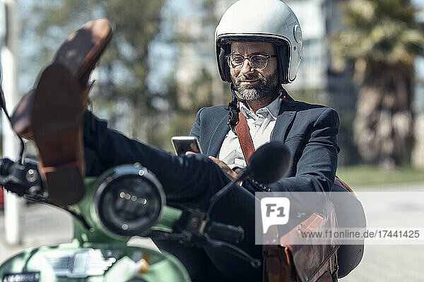 Male professional using mobile phone while sitting with feet up on scooter