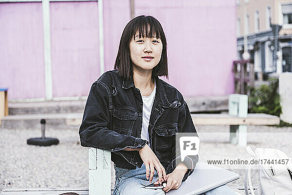 Female teenager with laptop sitting on bench