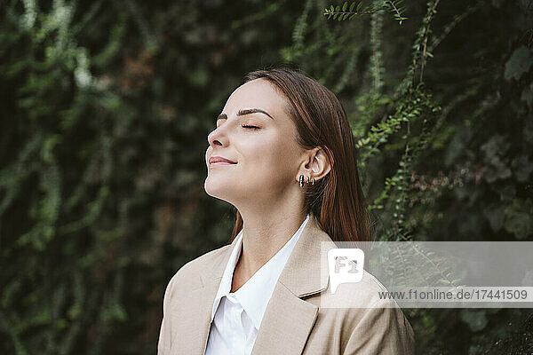 Businesswoman with eyes closed at green plant wall
