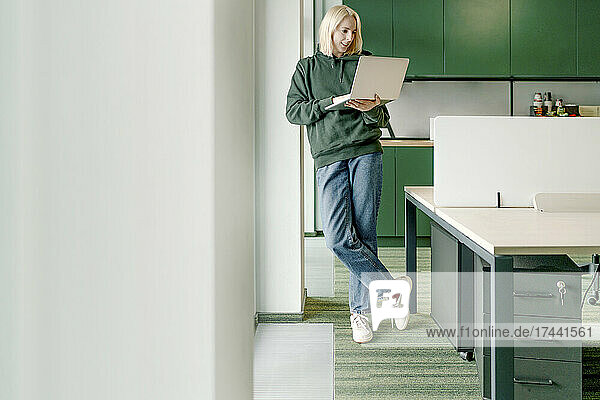 Businesswoman using laptop while leaning on architectural column in office