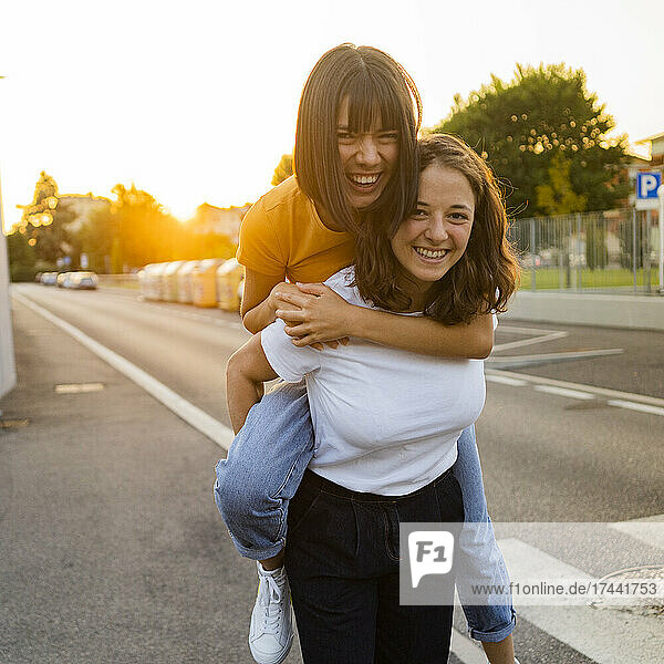 Happy woman giving piggyback ride to girlfriend on road