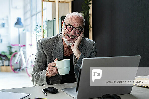 Glücklicher älterer Geschäftsmann mit Kaffeetasse am Arbeitsplatz