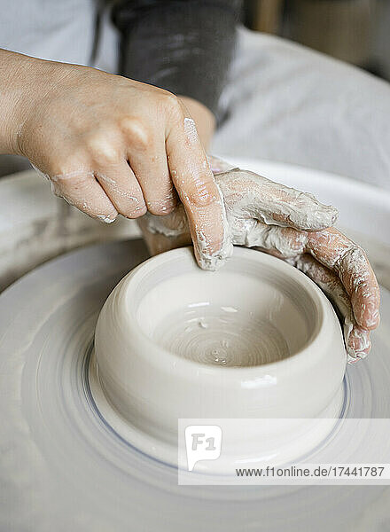 Young craftswoman molding clay with finger on pottery wheel