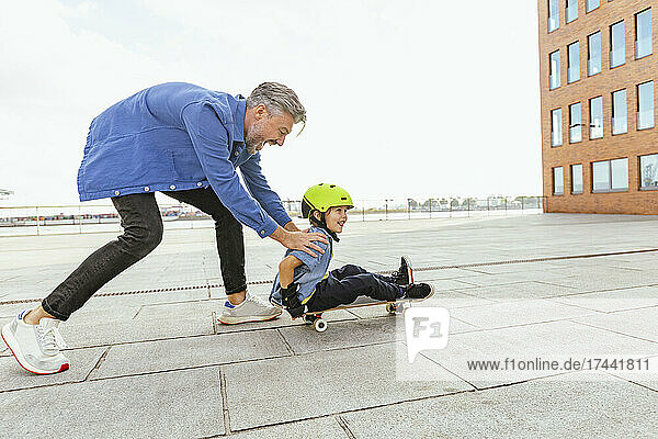Happy father playing with son sitting on skateboard