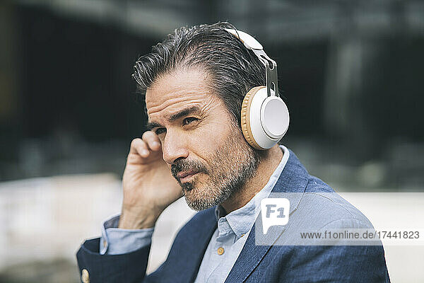 Mature male professional listening music through wireless headphones at hotel