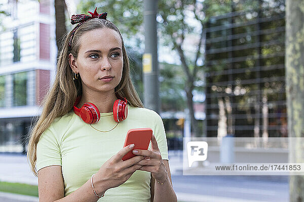 Young woman with wireless headphones holding smart phone