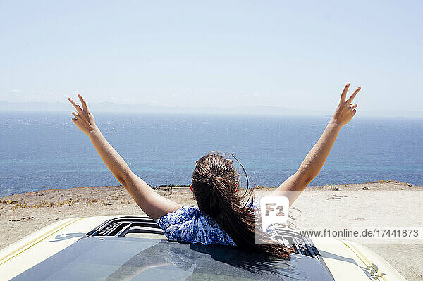 Carefree woman gesturing peace sign through sunroof of van during sunny day