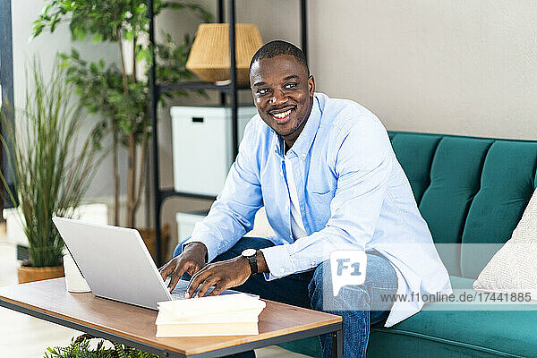Happy male professional with laptop sitting on sofa at home