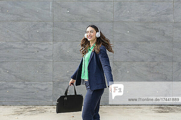 Happy businesswoman enjoying music through wireless headphones while walking