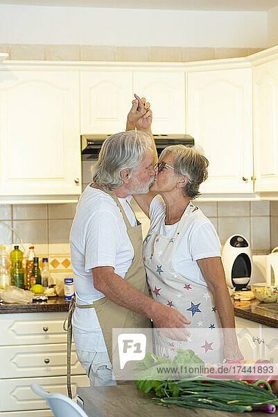 Senior couple holding hands while kissing in kitchen