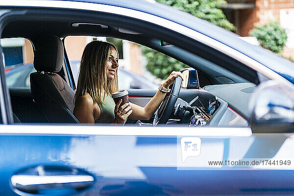 Blond woman with coffee cup driving car