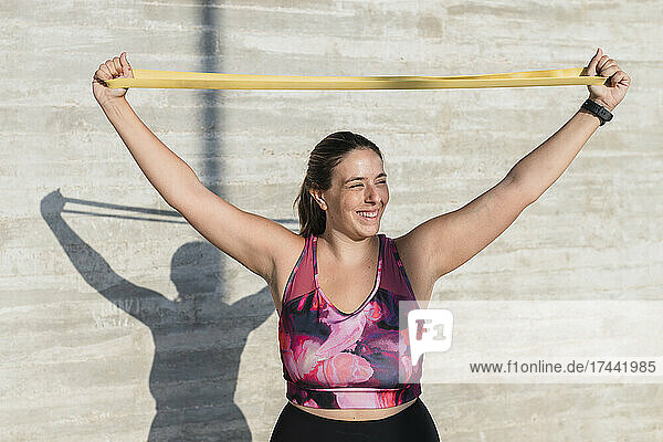Happy female athlete stretching resistance band while exercising during sunny day